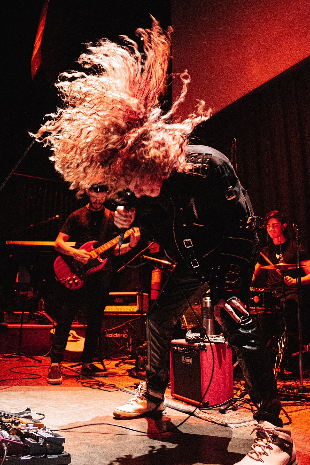Independent musician performing live on a small stage, bathed in stage lights, with an engaged audience in the foreground.
